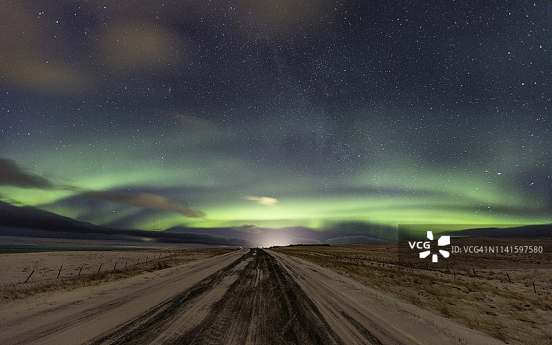 在冰岛，北极光照亮了一条荒芜的冰雪公路上的天空图片素材