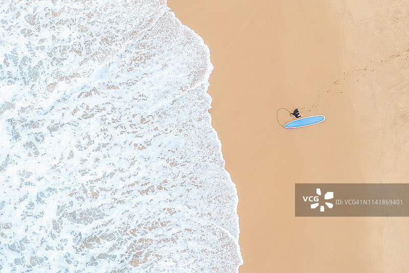 空荡的海滩和海浪的鸟瞰图。一个年轻人在海滩上冲浪。图片素材