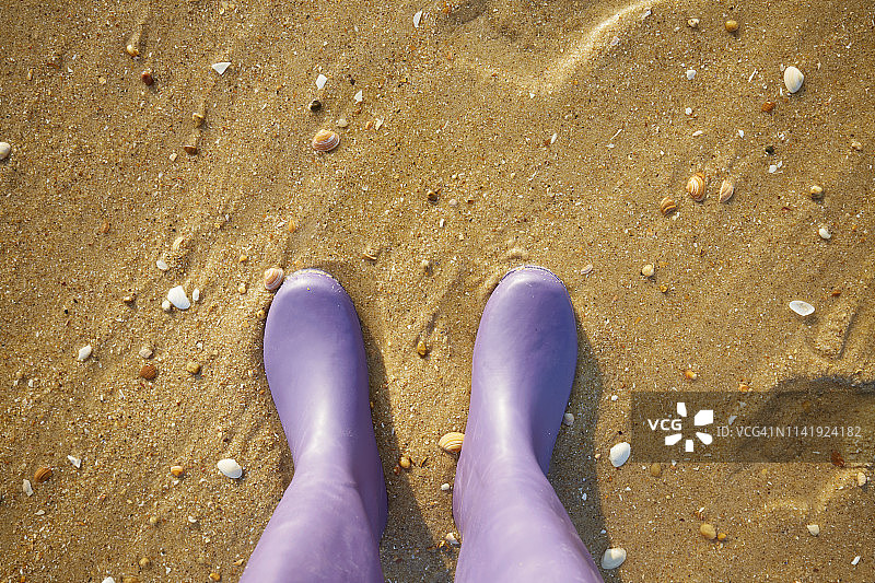 个人视角的女人站在紫色胶靴的沙滩上，低截面图片素材