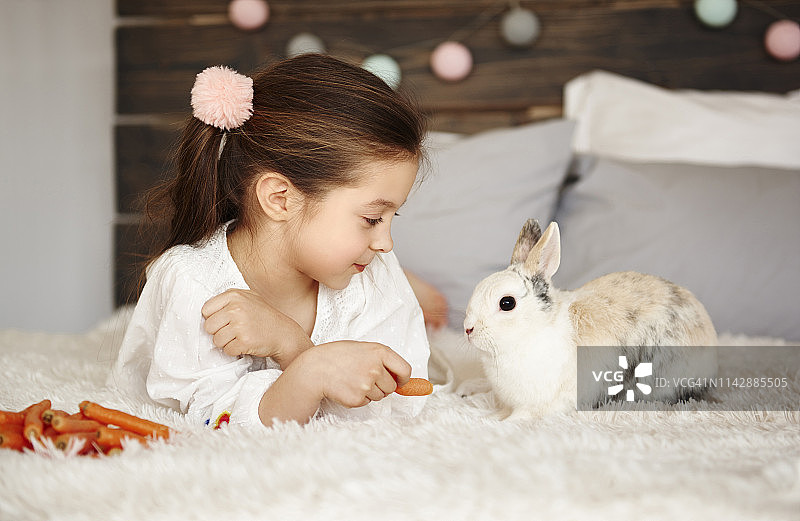 女孩躺在床上喂兔子。Debica、波兰图片素材