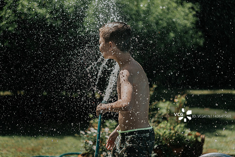 男孩在后院用水管泼水图片素材