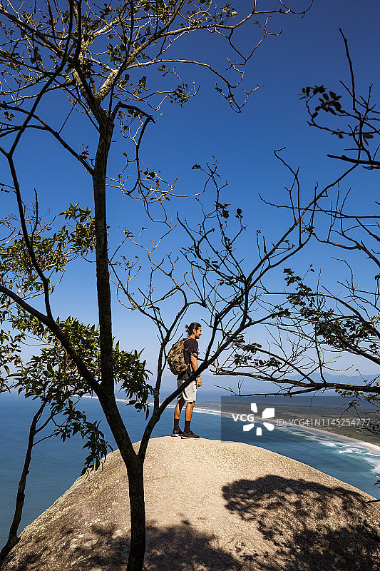 整个背包客站在悬崖上，背靠大海和蓝天图片素材