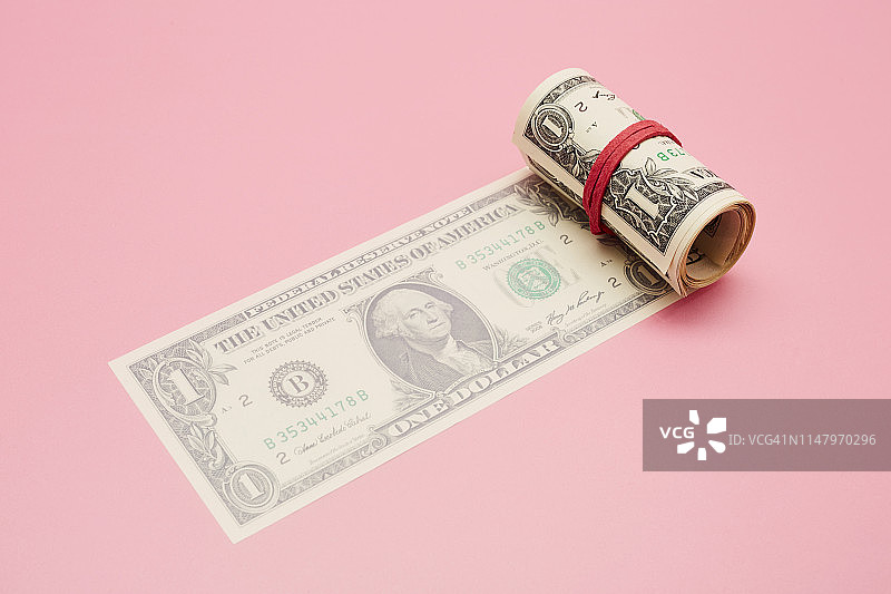 一卷粉红色背景的美元钞票图片素材