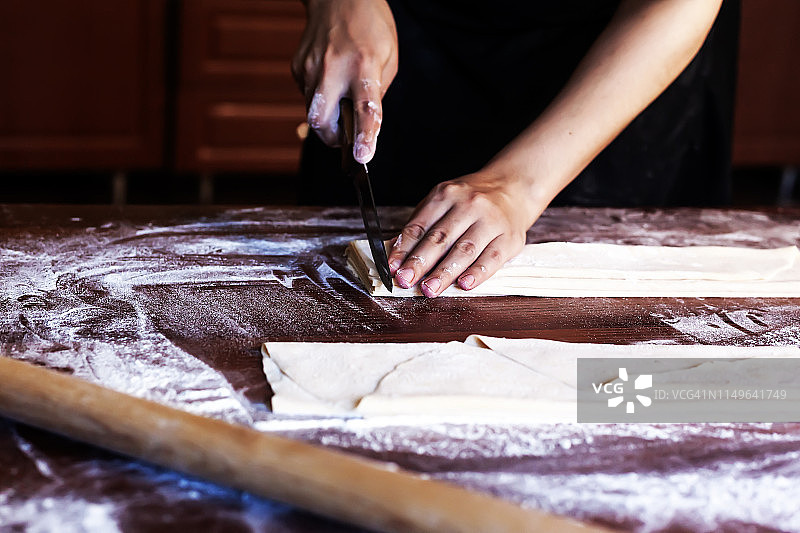 年轻的家庭主妇在厨房准备自制的意大利面。一名妇女正在为做意大利面而切割长条面团。图片素材