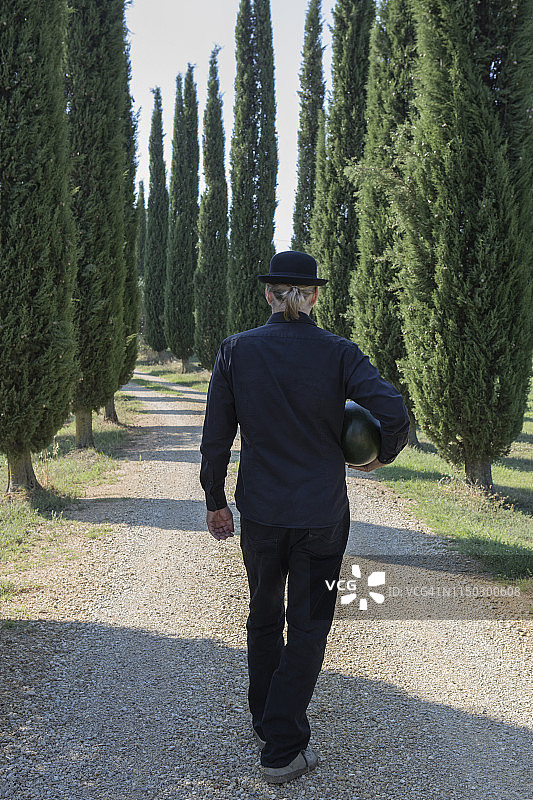 意大利托斯卡纳，后视图男子周围的柏树戴着一顶圆顶礼帽拿着一个甜瓜图片素材