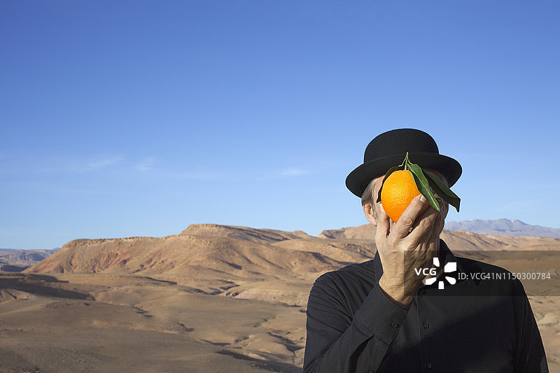 摩洛哥，乌尼拉谷，一名男子戴着圆顶礼帽，拿着一个橙子挡在面前图片素材