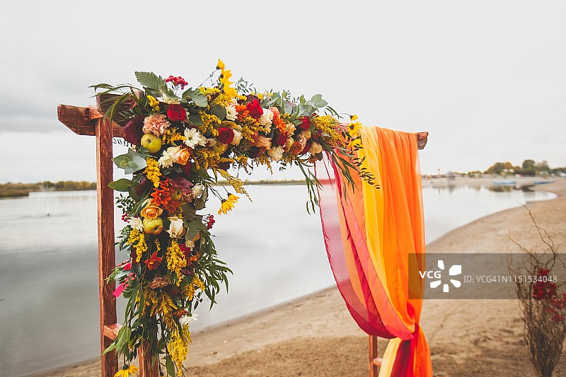 精致明亮的婚礼拱门鲜花和织物在沙滩上的河流或湖泊。美丽的秋天装饰，婚礼装饰。婚礼地点在海滩上图片素材