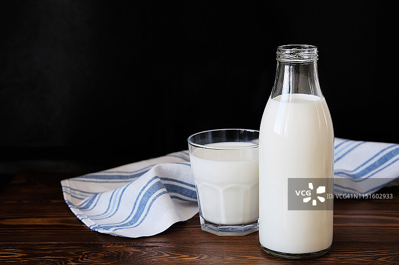 新鲜牛奶装在玻璃瓶和马克杯里，放在一张木桌上，旁边是一条亚麻条纹毛巾。健康有机理念，农产品。乡村风格的静物生活。为文本复制空间。图片素材