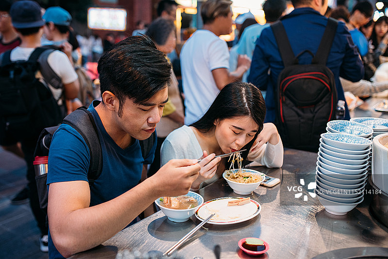可爱的年轻亚洲夫妇在台北夜市享受街头小吃。图片素材