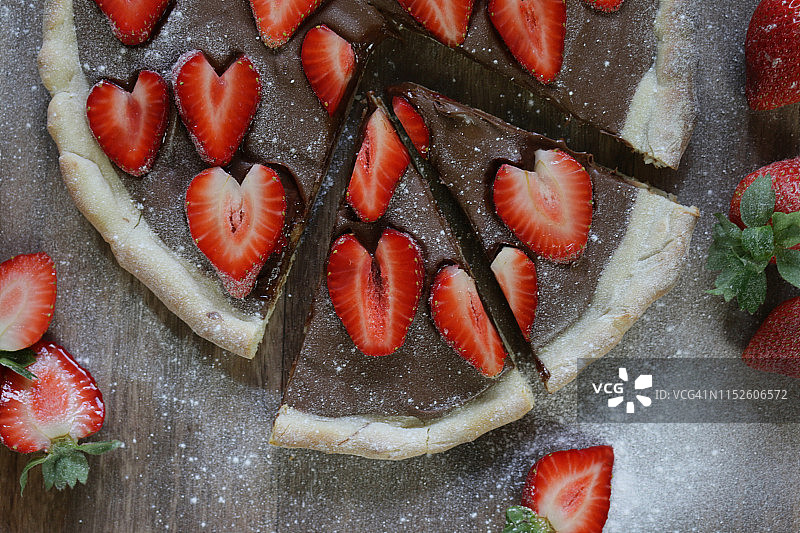 这是一个用草莓和糖霜自制的巧克力披萨，烤披萨的外皮上涂满榛子巧克力，上面是浪漫的红色心形草莓/草莓水果，可以切成薄片当布丁吃图片素材