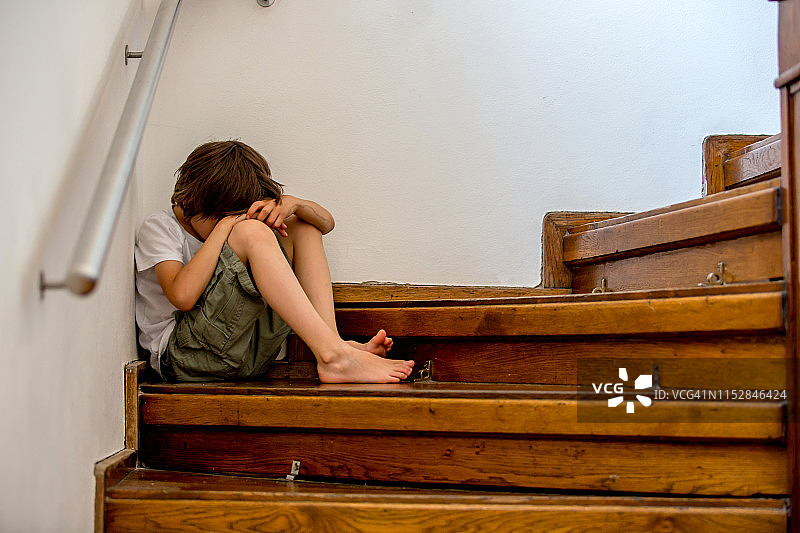 悲伤的孩子，坐在大房子的楼梯上，恃强凌弱的概念图片素材