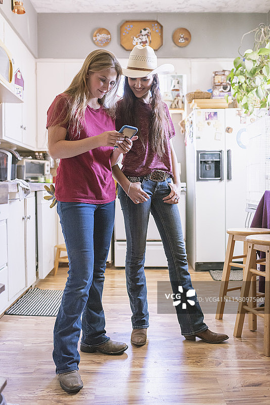 两个十几岁的女孩在房子的厨房里看手机图片素材