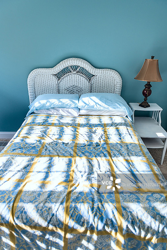 干净的床，床头板、床头柜、床头灯和卧室里的复古海滩主题装饰蓝色枕头，以及从窗户射进来的阳光阴影图片素材