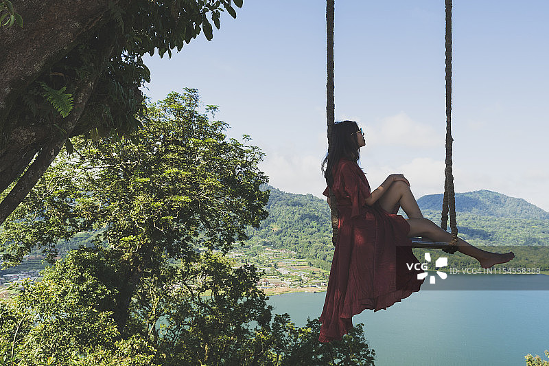 女孩坐在秋千上对着Buyan湖，贝杜古尔，印度尼西亚巴厘岛图片素材