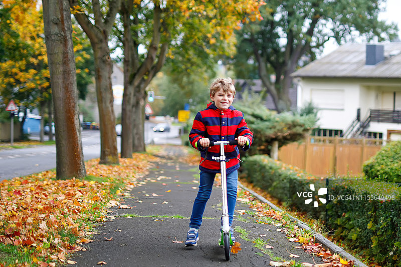 可爱的小男孩骑着滑板车在街道和城市的人行道上行走。儿童在冬天、春天或秋天进行户外活动。滑稽快乐的孩子穿着五颜六色的时装图片素材