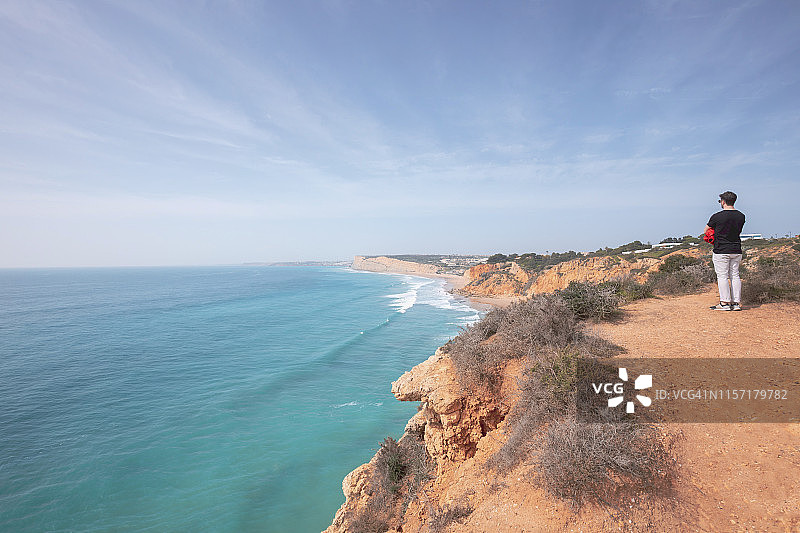 葡萄牙，阿尔加维，拉各斯，蓬塔·达·皮达德，一个人站在海岸边望着大海图片素材
