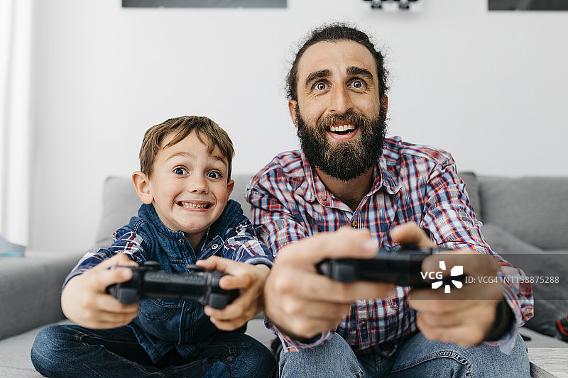 父亲和儿子一起坐在沙发上玩电脑游戏的肖像图片素材