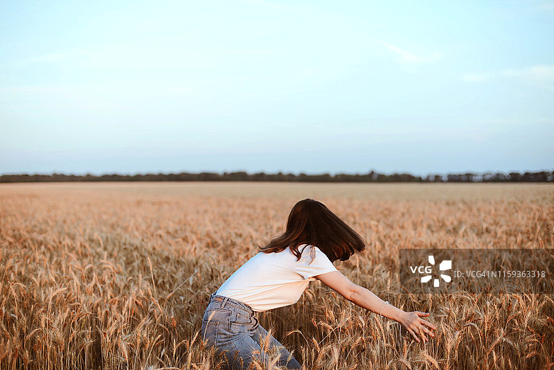 一幅年轻女子的画像，她站在麦田里，背对着天空图片素材