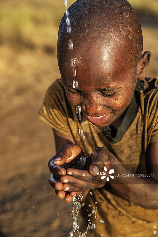 非洲小男孩在非洲东部的稀树草原上喝着淡水图片素材