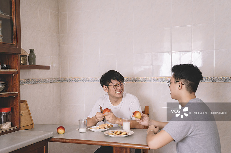 2个亚洲华人兄弟姐妹早上上班前在厨房的餐桌上吃早餐图片素材