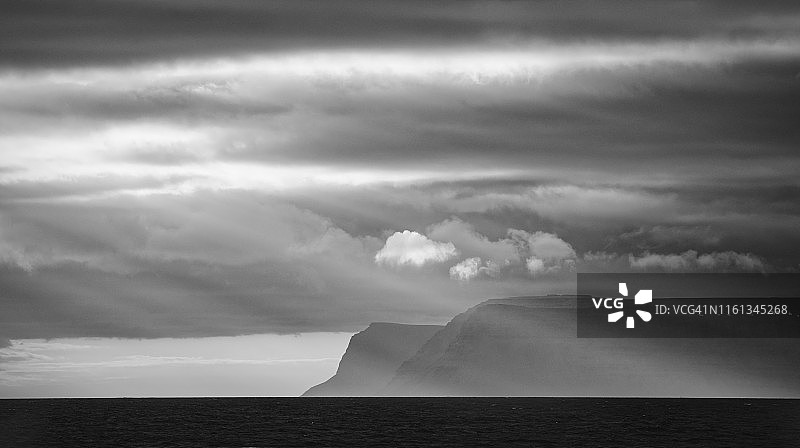 戏剧性的阳光在黑和白色的山脉沿西峡湾海岸线，冰岛图片素材