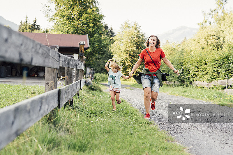 快乐的母亲和女儿在奥地利约赫贝格的乡村小路上奔跑图片素材