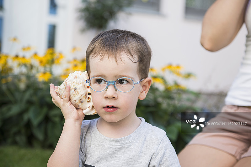 德国巴伐利亚，一个男孩在屋外听贝壳声图片素材