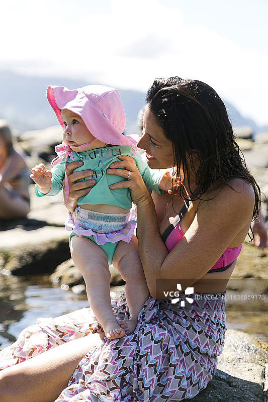 一个女人抱着婴儿的女儿站在海滩的岩石上图片素材