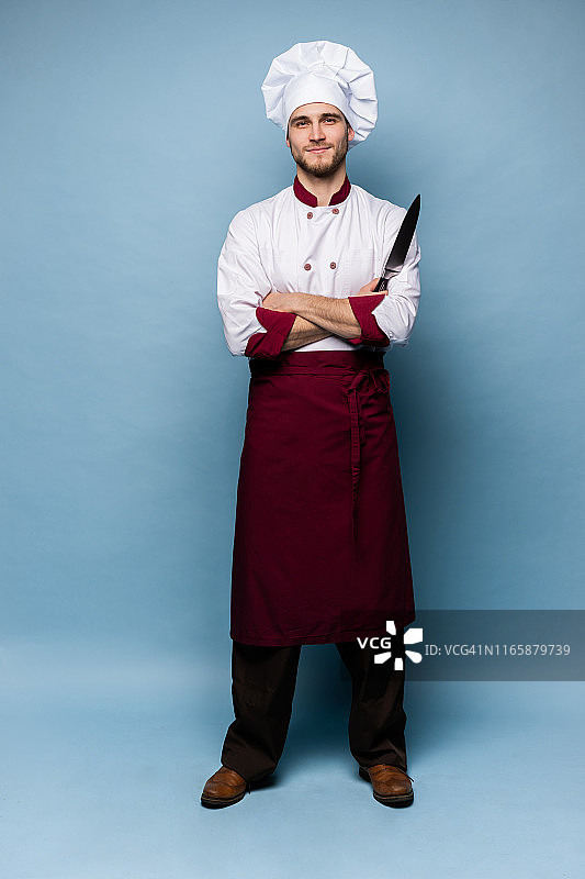 英俊的男厨师厨师拿着刀孤立在浅蓝色的背景。图片素材
