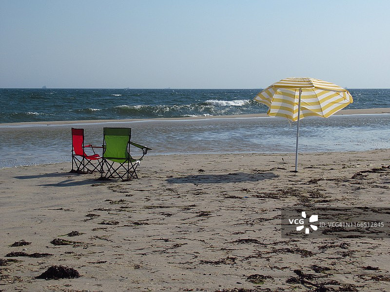 夏天，水边的沙滩上放着两把沙滩椅和一把雨伞图片素材