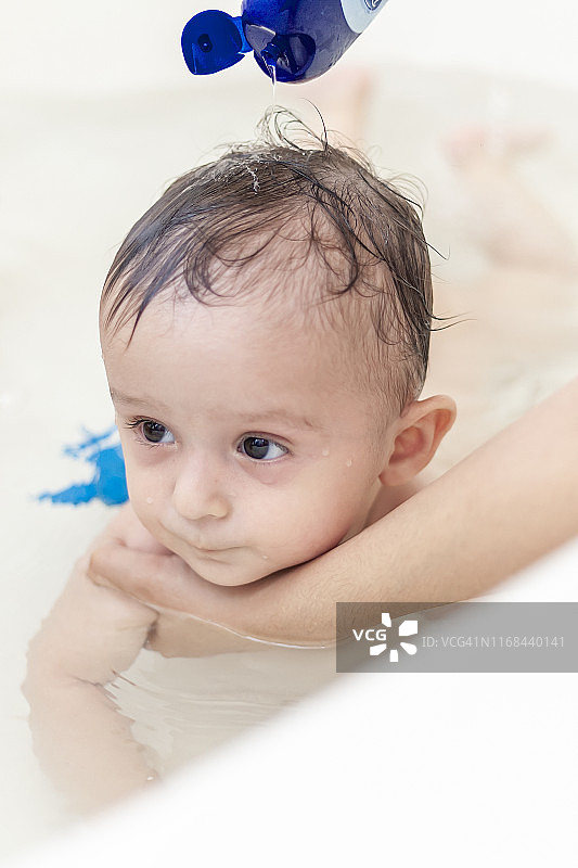 一位年轻的妈妈在浴室里给她的小儿子洗头。妈妈给宝宝洗澡图片素材