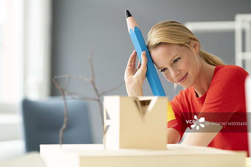办公室里的年轻女子桌上放着大号钢笔和建筑模型图片素材