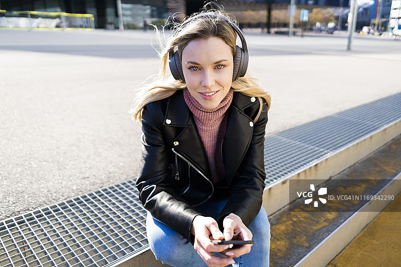 西班牙巴塞罗那，年轻女子用智能手机和耳机听音乐的肖像图片素材