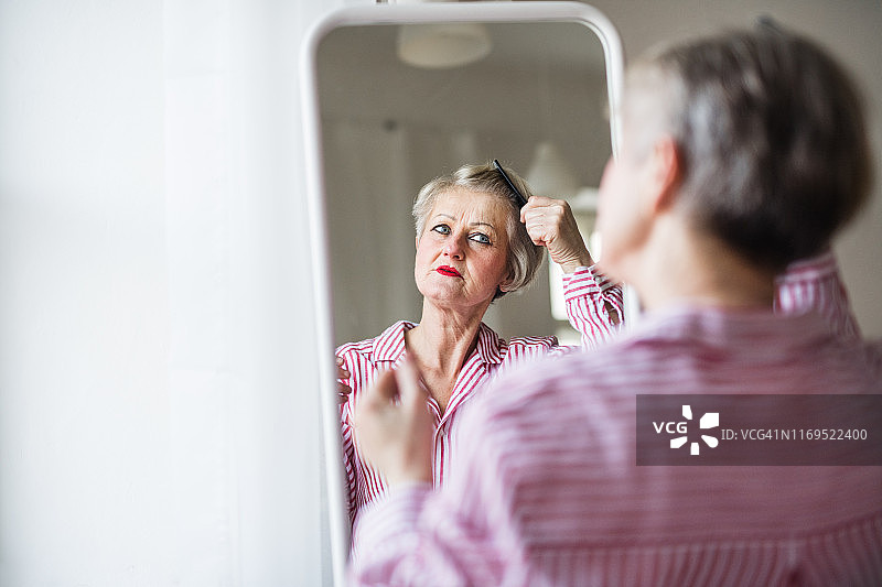 一位活跃的老年妇女在室内梳头，看着镜子。图片素材