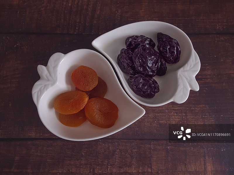 秋天的水果:一堆杏干和梅干，放在一个旧木桌上的心形瓷碗里图片素材
