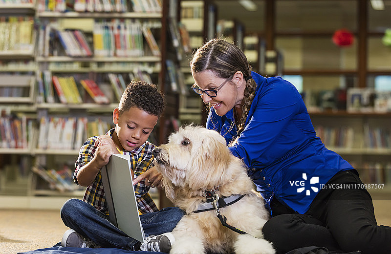 混血男孩在图书馆阅读与治疗狗图片素材