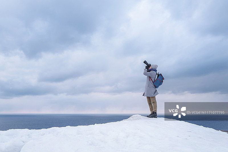 摄影师在白雪覆盖的山上拍摄照片，背后是纯净的海洋和天空图片素材