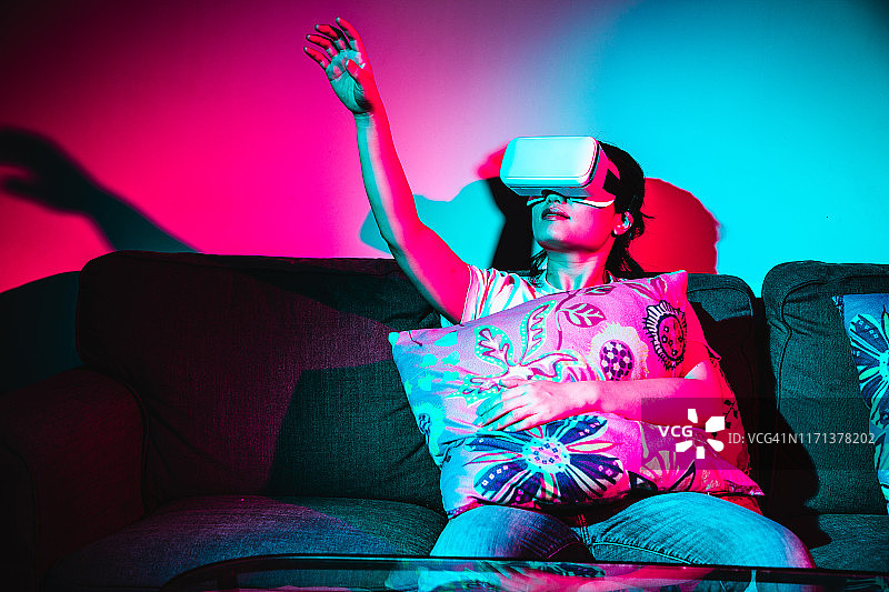 女人使用虚拟现实耳机和放松在沙发上图片素材