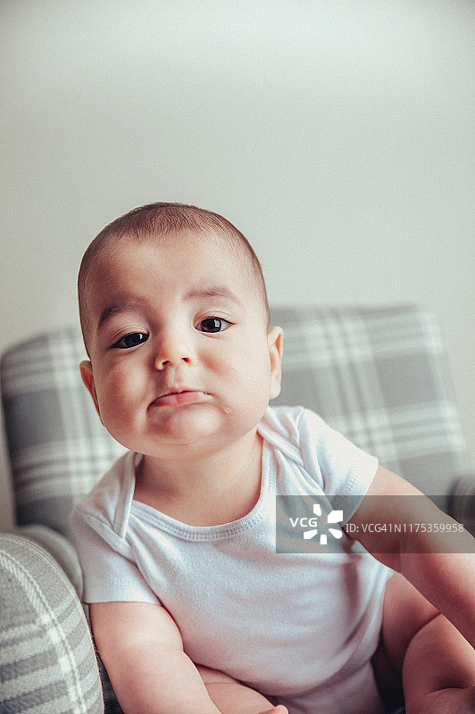 7个月大的男婴穿着白色连体衣坐在格子摇椅和地毯上图片素材
