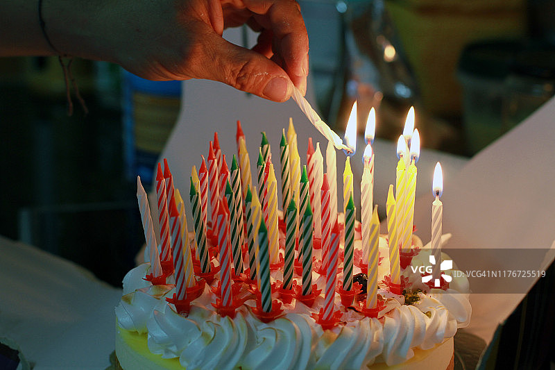 手在生日蛋糕上点燃蜡烛图片素材