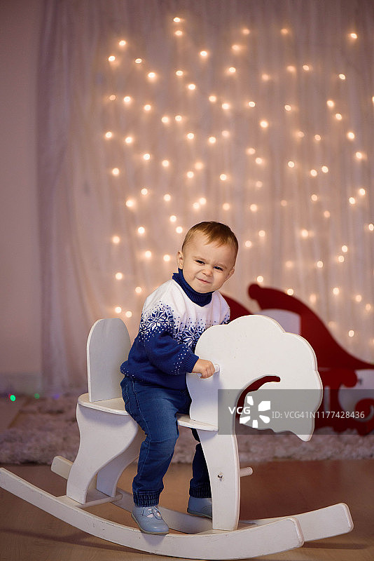 小男孩在家里玩玩具，在室内。五彩缤纷的圣诞彩灯背景。家庭、假日、生活理念。图片素材