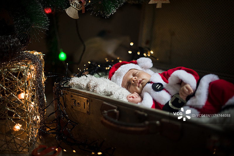 新生儿在圣诞老人的衣服躺在圣诞树下。图片素材