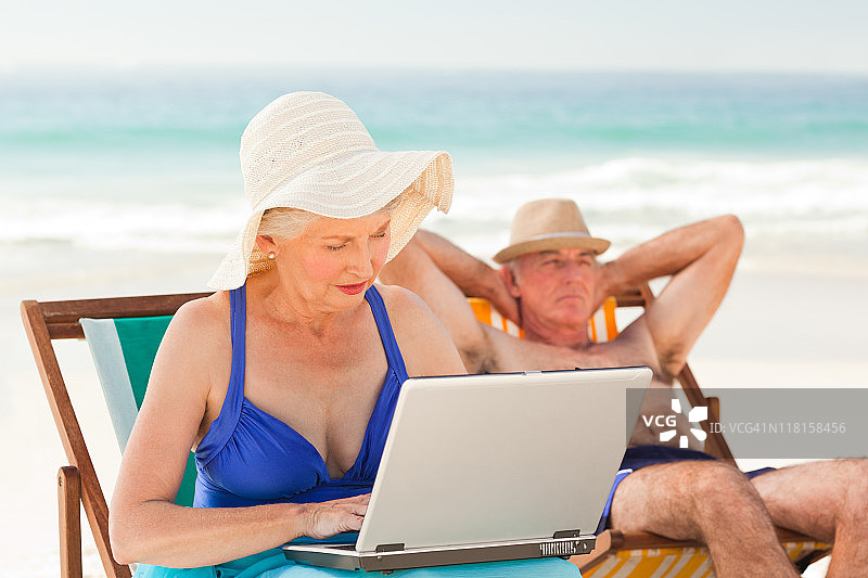 当丈夫在海滩上睡觉时，一个女人却在用笔记本电脑工作图片素材
