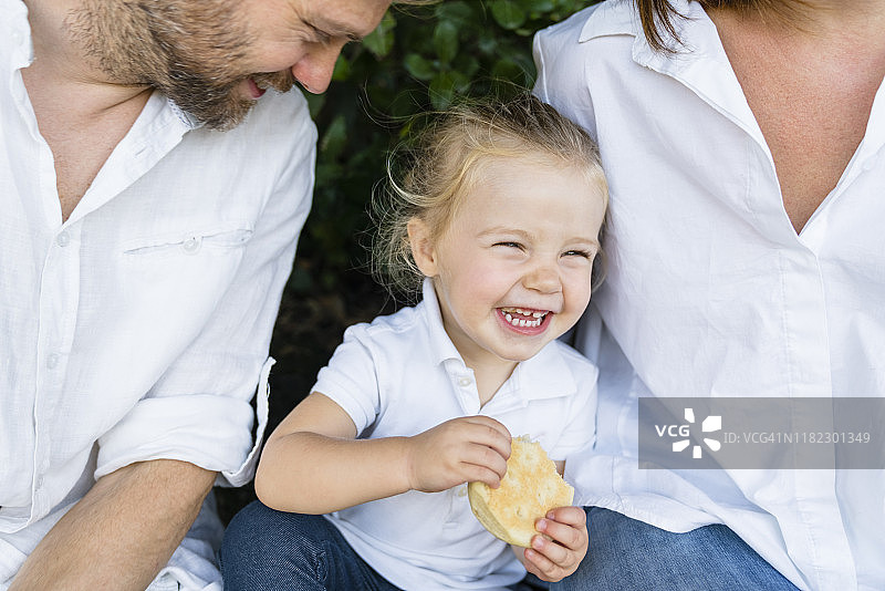 快乐的小女孩拿着零食坐在父母中间图片素材