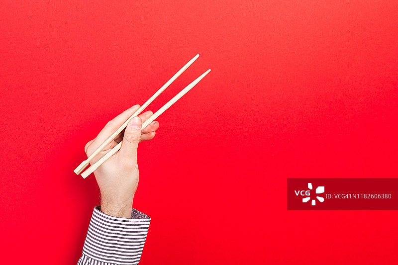 用筷子夹着的男性的手放在红色的背景上。传统亚洲食物与空空间为您的设计图片素材