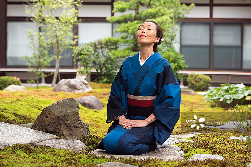 成熟的日本妇女穿着传统和服跪在京都寺庙花园图片素材