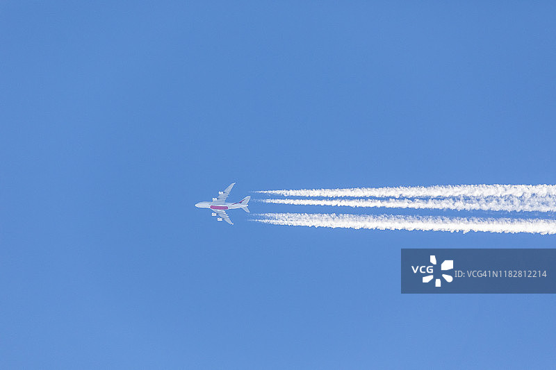 在晴朗的蓝天下，有蒸汽尾迹的飞机。图片素材