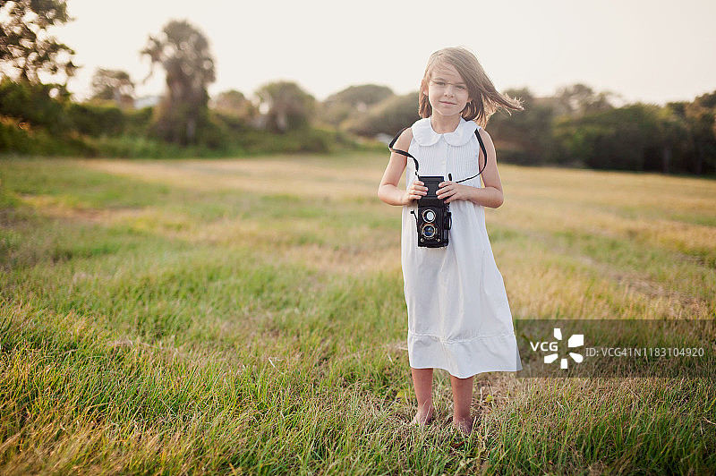 美国南卡罗来纳州查尔斯顿，一个女孩拿着一台老式相机站在田野里图片素材