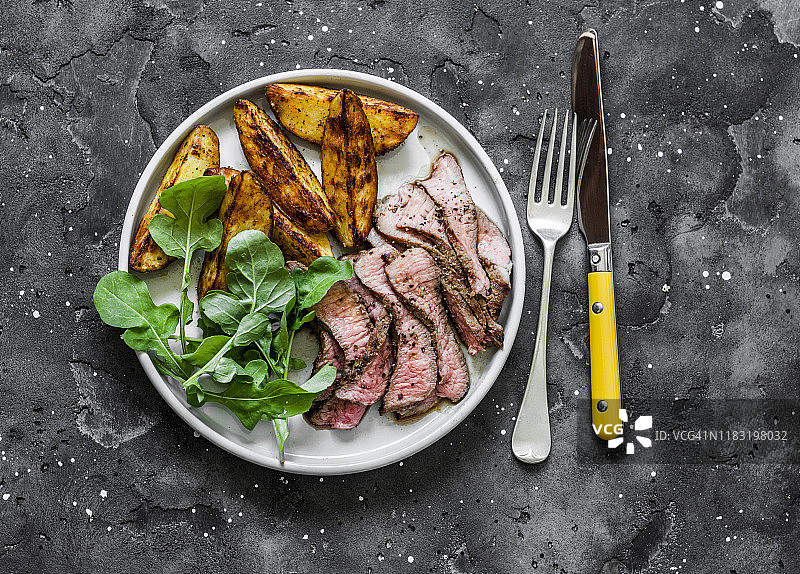 牛排和烤新土豆-美味的午餐在一个黑暗的背景，俯视图图片素材