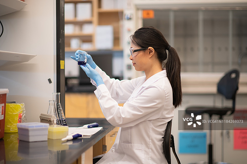 一位亚洲生物化学家正在烧杯中检验一种蓝色化学物质图片素材